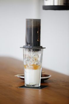 A refreshing iced coffee prepared with an Aeropress, milk, and ice on a warm-toned wooden table.