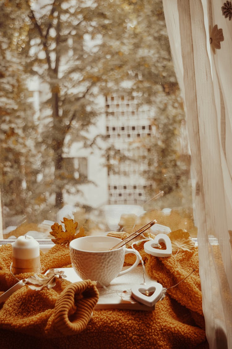 Teacup Beside A Candle On A Table By The Glass Window