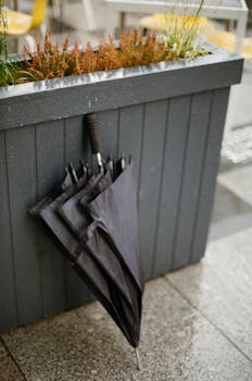 A folded black umbrella leaning against a city planter box on a wet tiled surface.