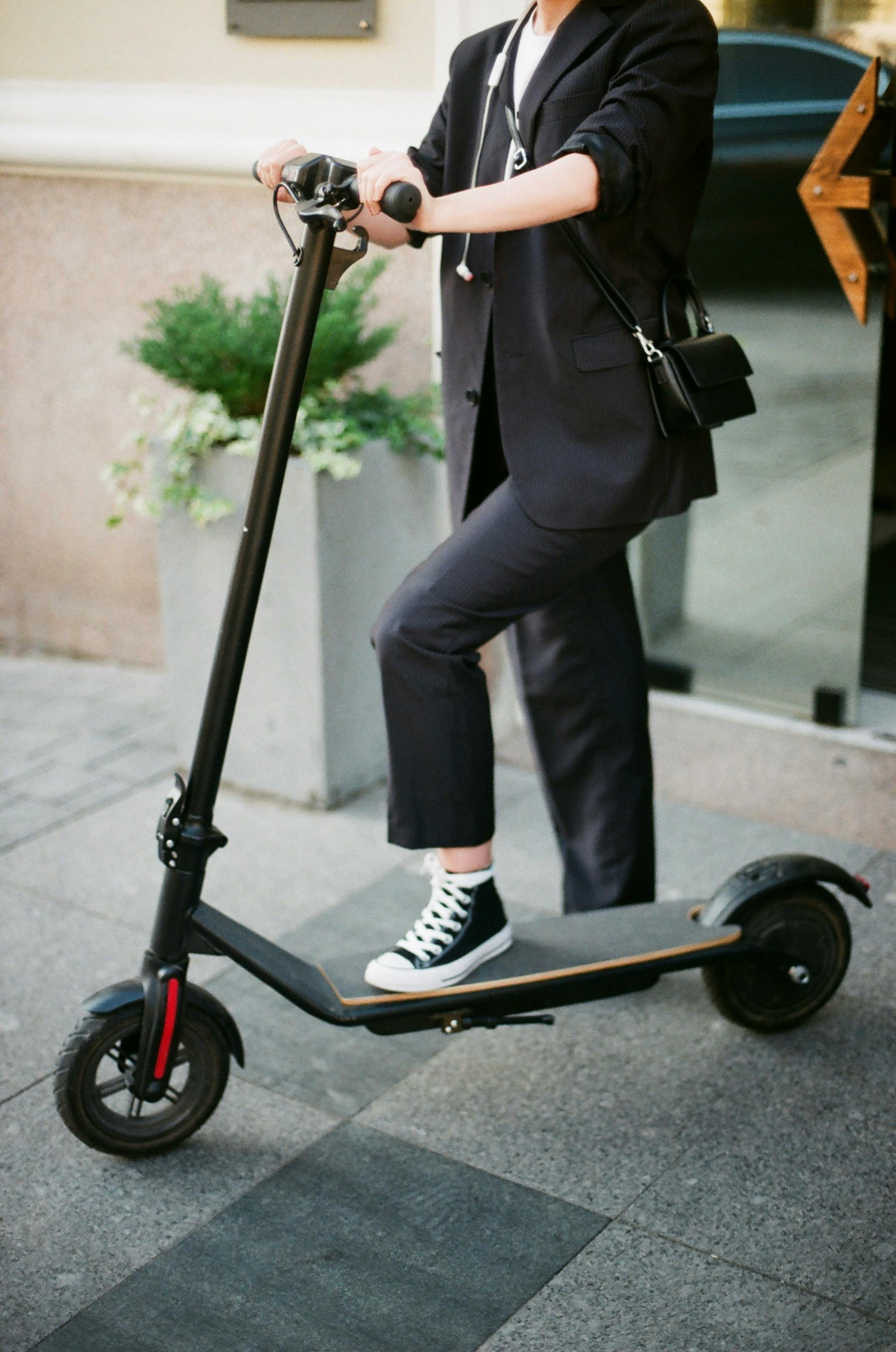 unrecognizable woman wearing office suit and converse stepping on scooter