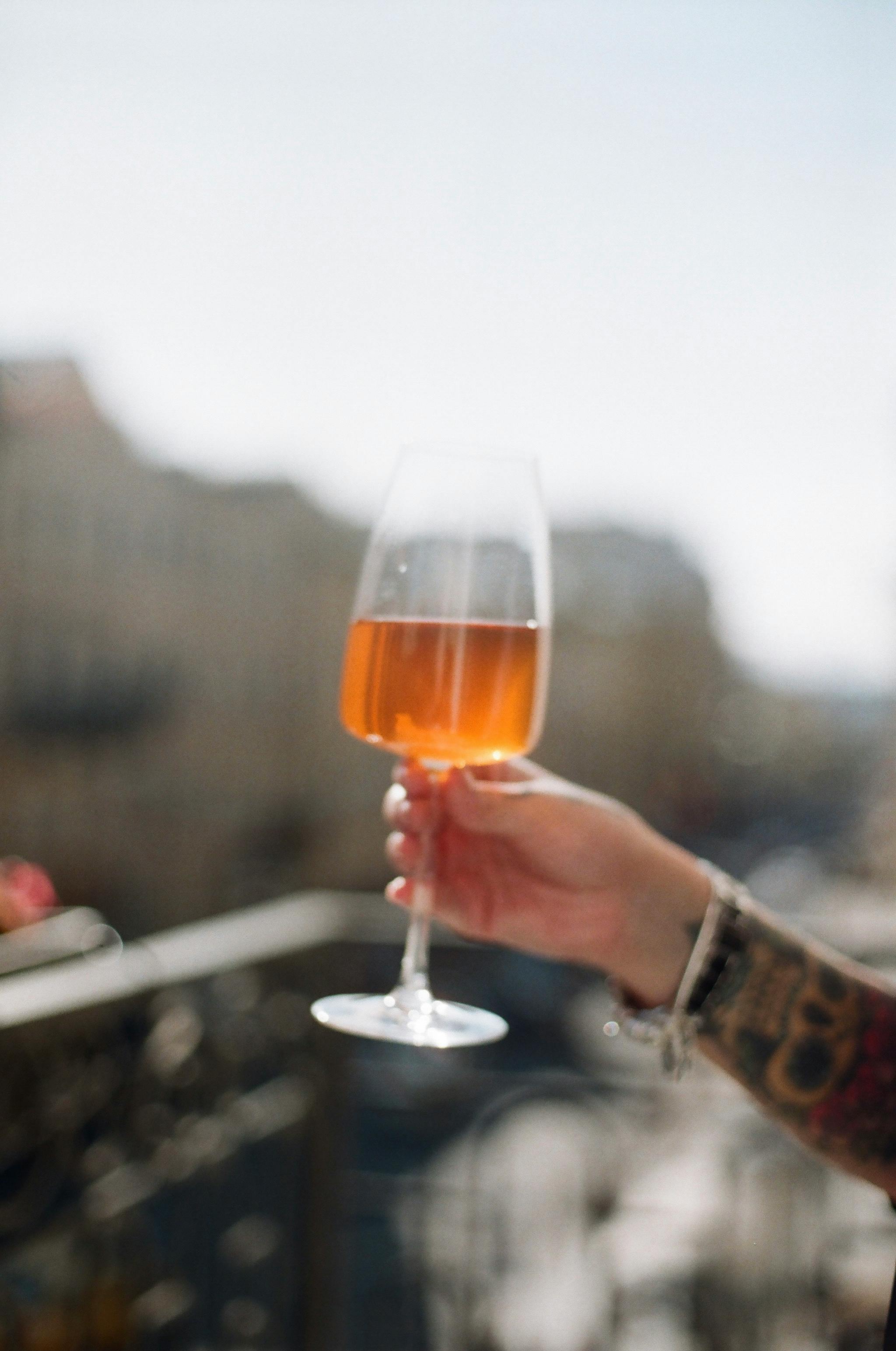 A tattooed hand holds a wine glass against a blurred city backdrop, capturing a moment of leisure.