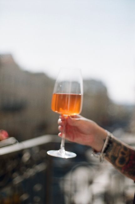 A tattooed hand holds a wine glass against a blurred city backdrop, capturing a moment of leisure.