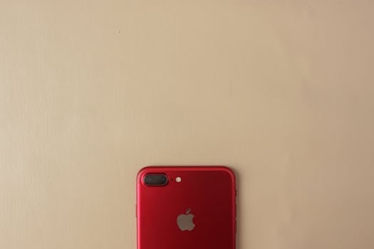 Minimalist photo of a red smartphone on a beige surface, ideal for tech or lifestyle themes.