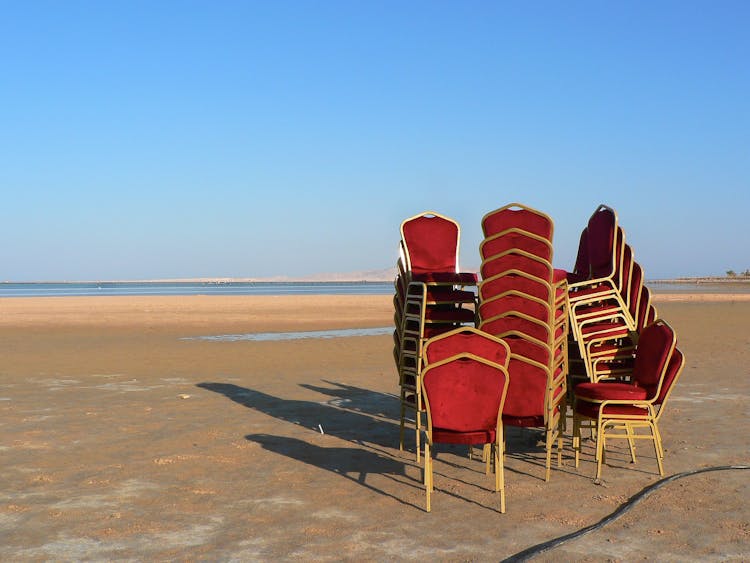 Antique Chairs Stacked On Each Other On The Beach 