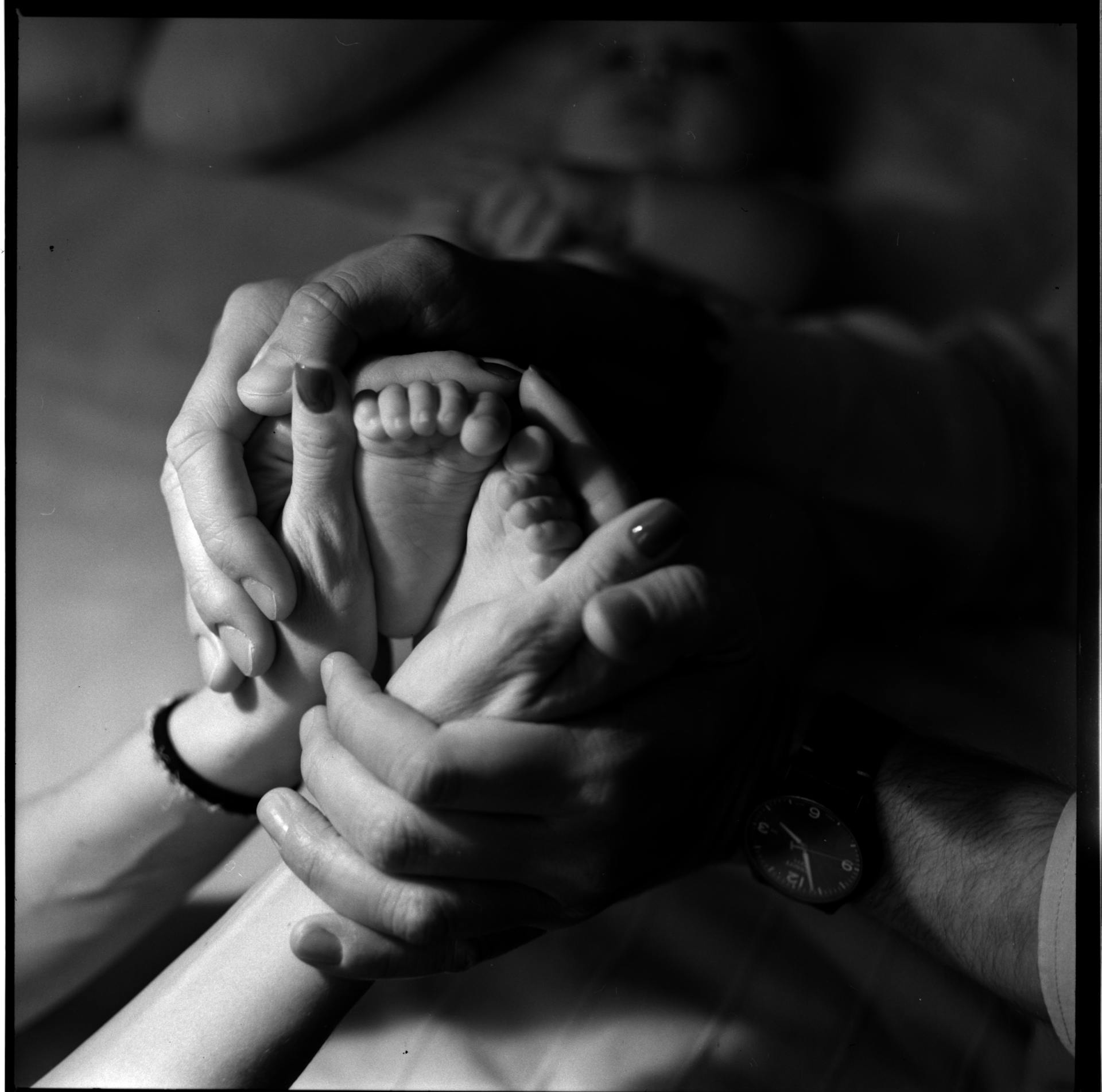 Tender black and white image of a baby's feet cradled in adult hands, symbolizing family love and care.