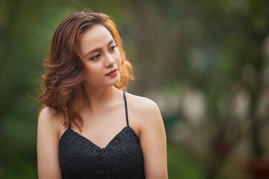 A serene outdoor portrait of a woman in a black lace dress, looking sideways.
