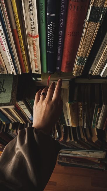 A hand reaches for a book on a crowded library bookshelf, evoking curiosity and exploration.