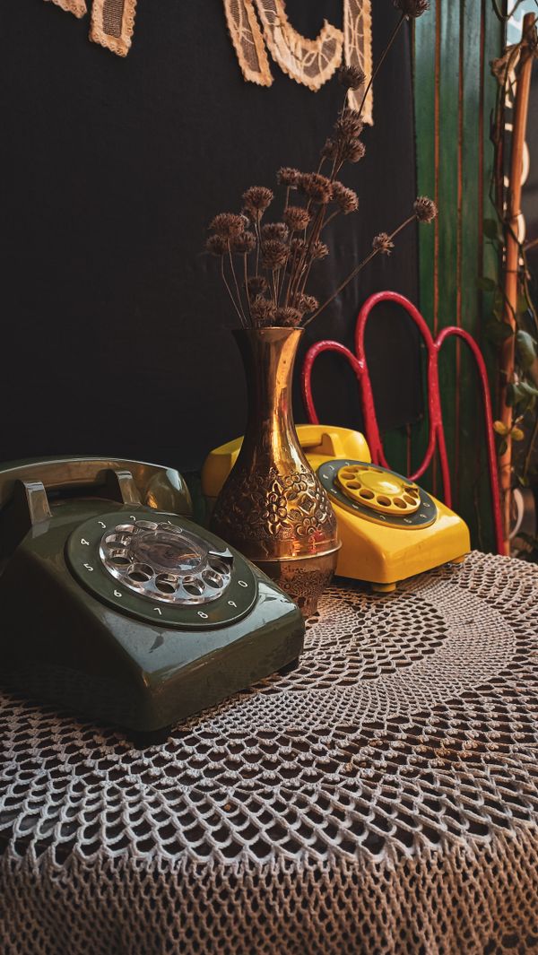 Vintage rotary telephones and a brass vase on lace, photo by Yesim Dereci on Pexels