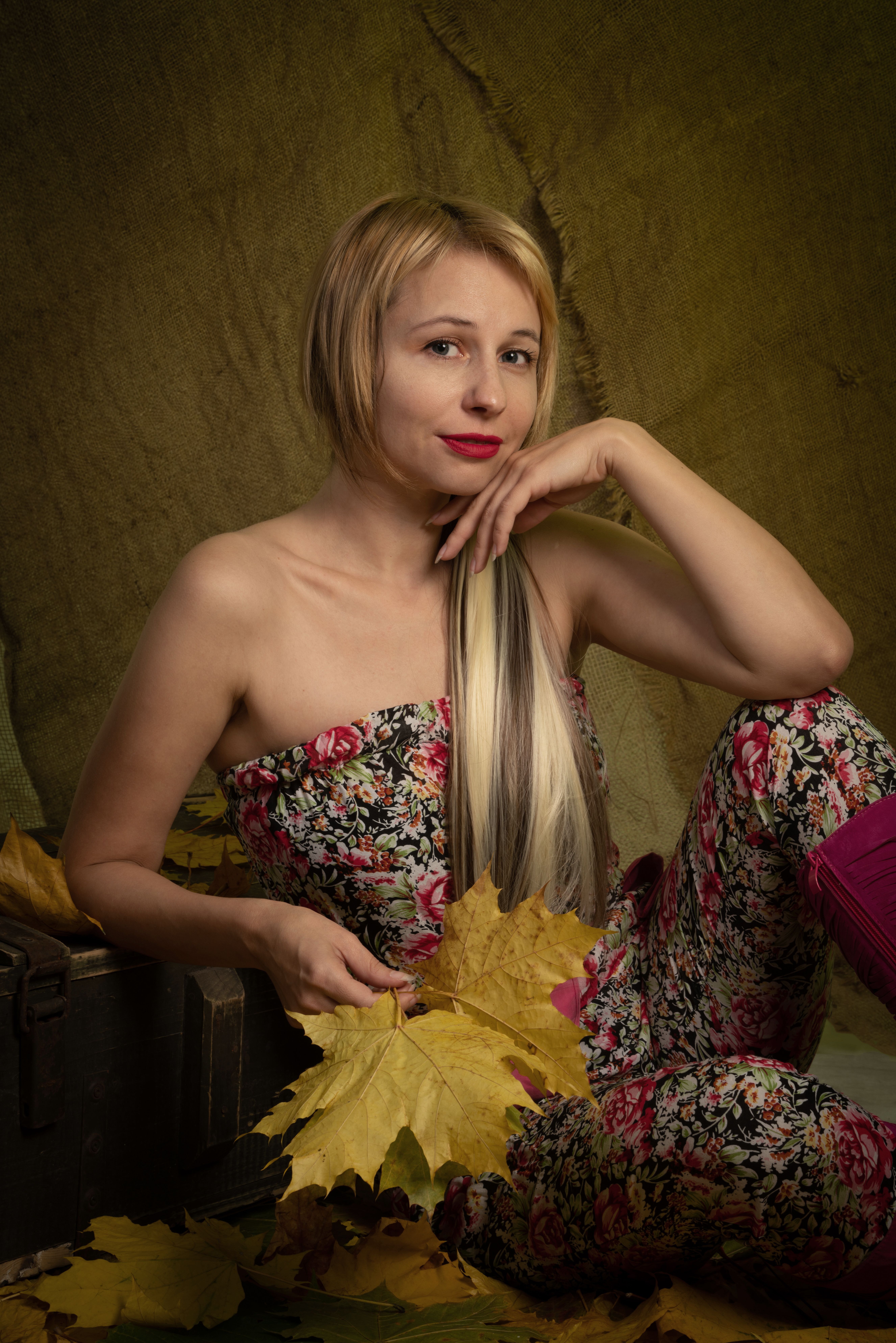 Elegant woman in floral outfit posing with autumn leaves, showcasing seasonal charm.