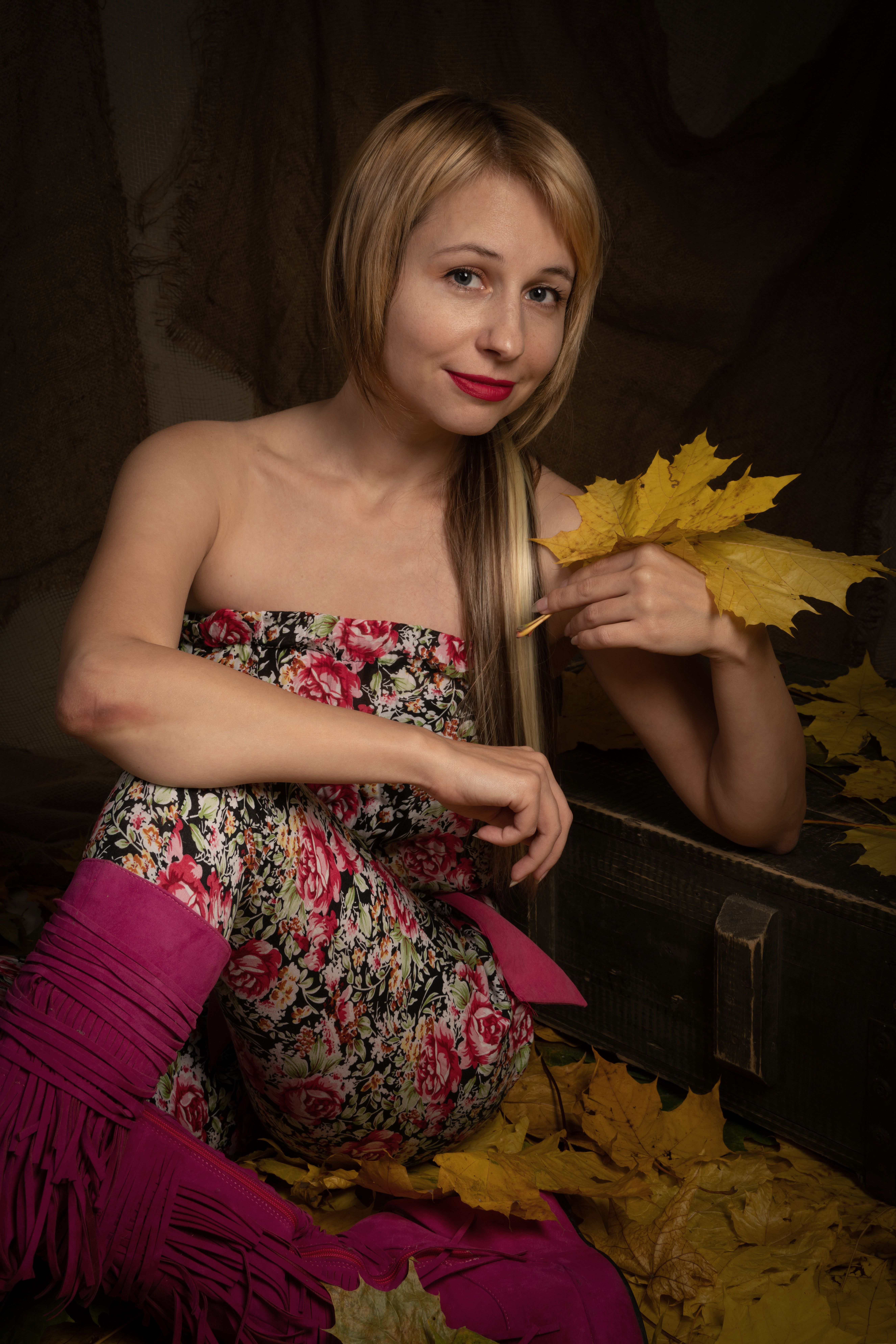Caucasian woman in floral outfit sitting with autumn leaves, indoors.