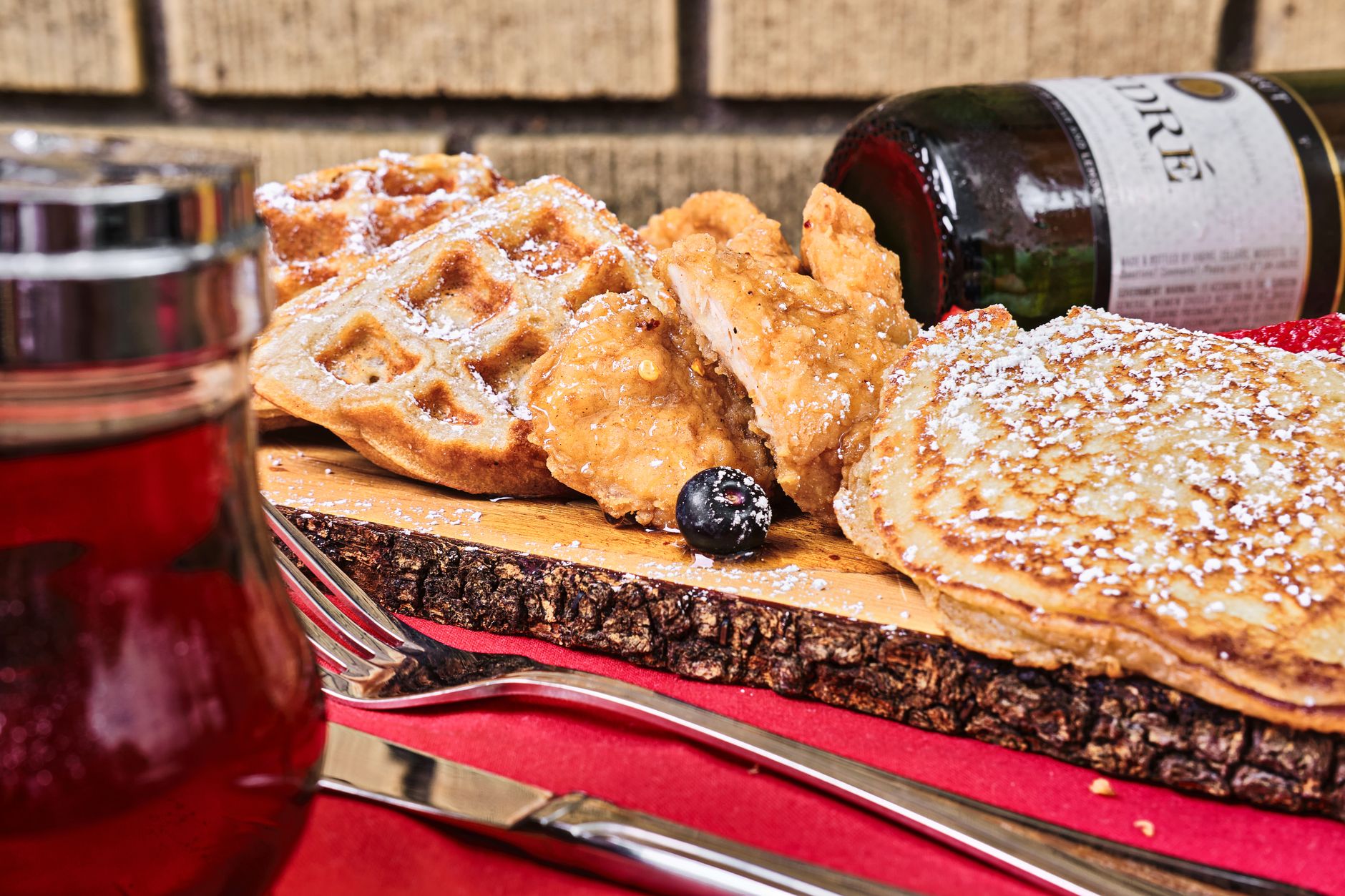 A savory breakfast spread featuring chicken, waffles, and pancakes on a rustic wooden board.