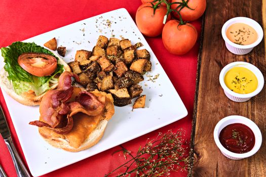 A tasty bacon cheeseburger served with roasted potatoes and assorted sauces for a delightful meal.
