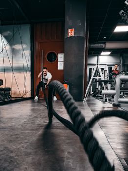 Man performing a high-intensity rope workout in a modern gym setting. Fitness and strength focus.