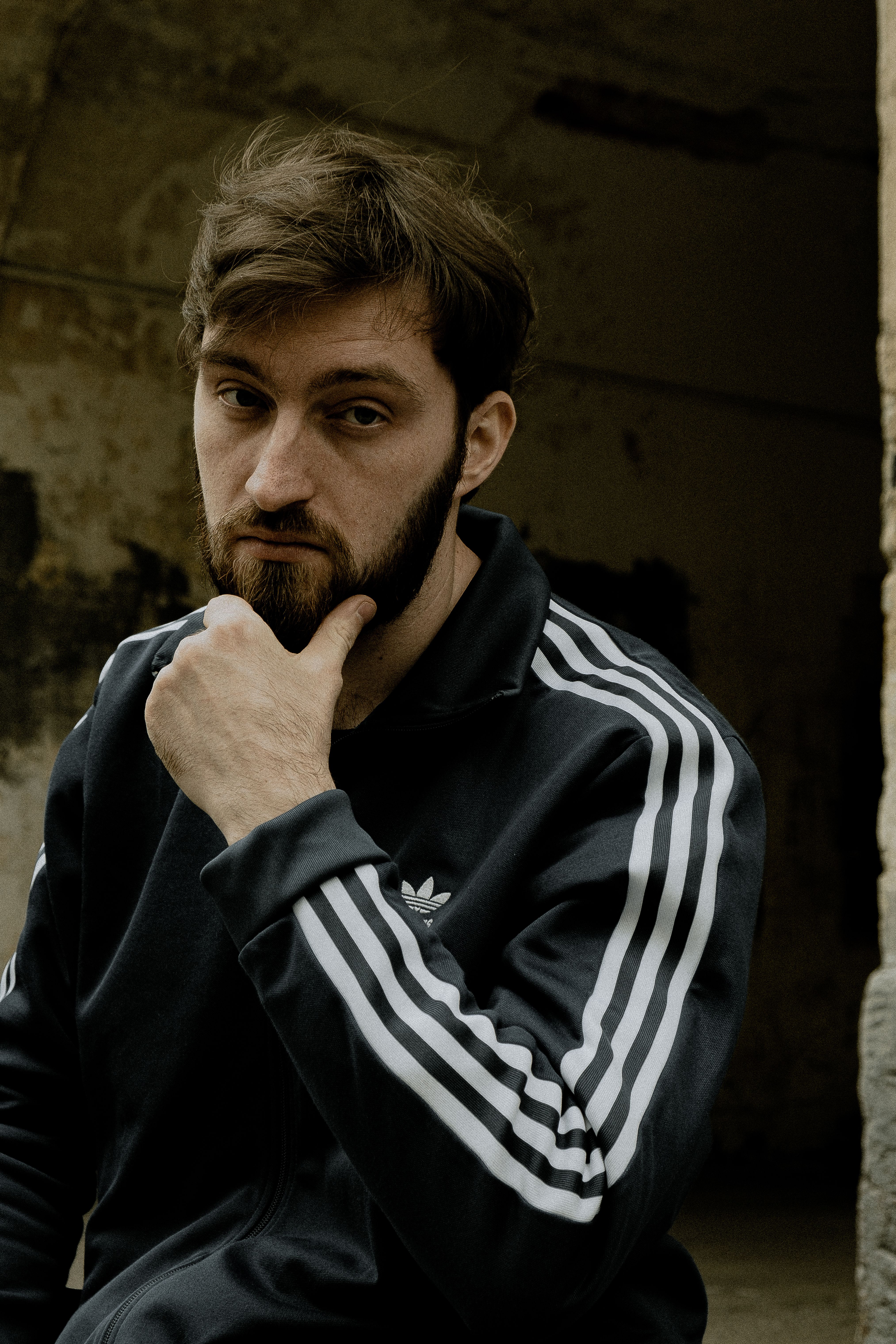 Bearded man in adidas sportswear posing seriously outdoors. Urban feel, confident expression.