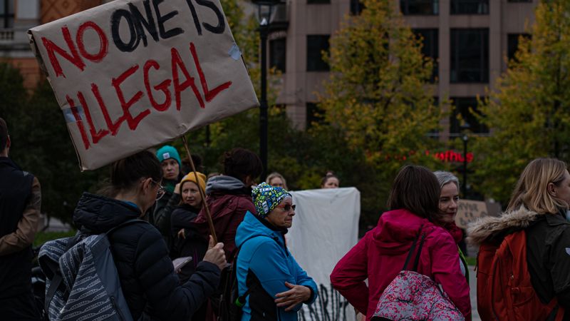 A group of diverse adults protesting immigration policies with signs outdoors.
