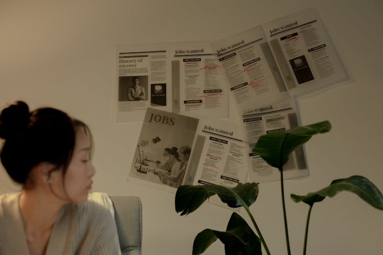 Woman Sitting And Looking Away With Job Postings Pinned On Wall