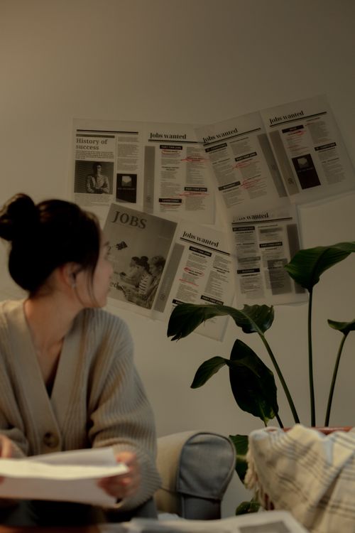 Free A woman in a cozy setting reviews job listings on a wall, exuding a thoughtful mood. Stock Photo