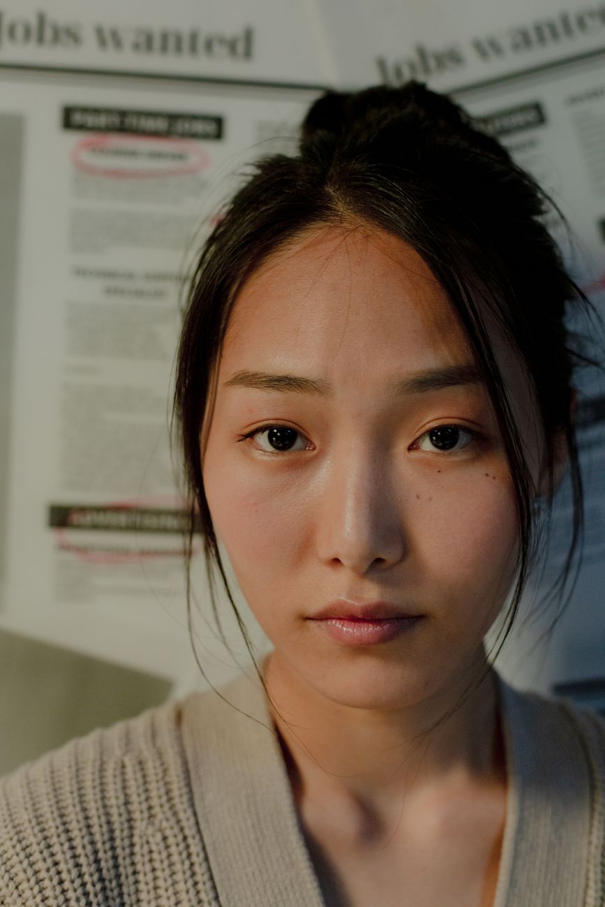 Portrait of a woman with black hair standing indoors by job listings, conveying introspection.