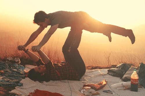 Free Woman Lying on Blanket Under Man on Her Legs Holding Hands during Golden Hour Stock Photo