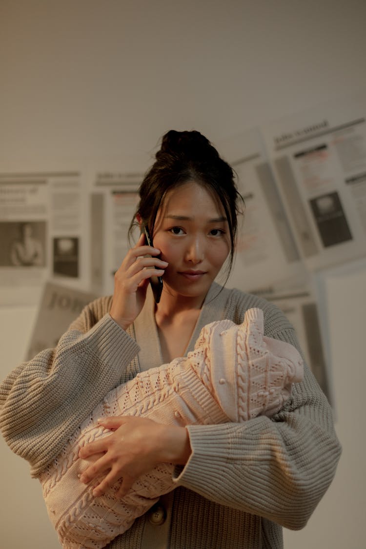 Woman Holding Newborn Baby And Talking On Phone