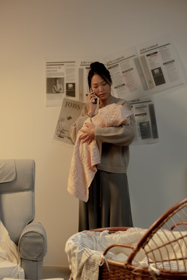 Woman Talking On Phone And Holding Newborn Baby In Hands