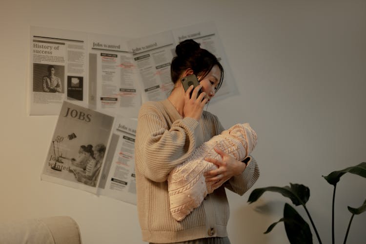 Woman Talking On Phone And Holding Newborn Baby