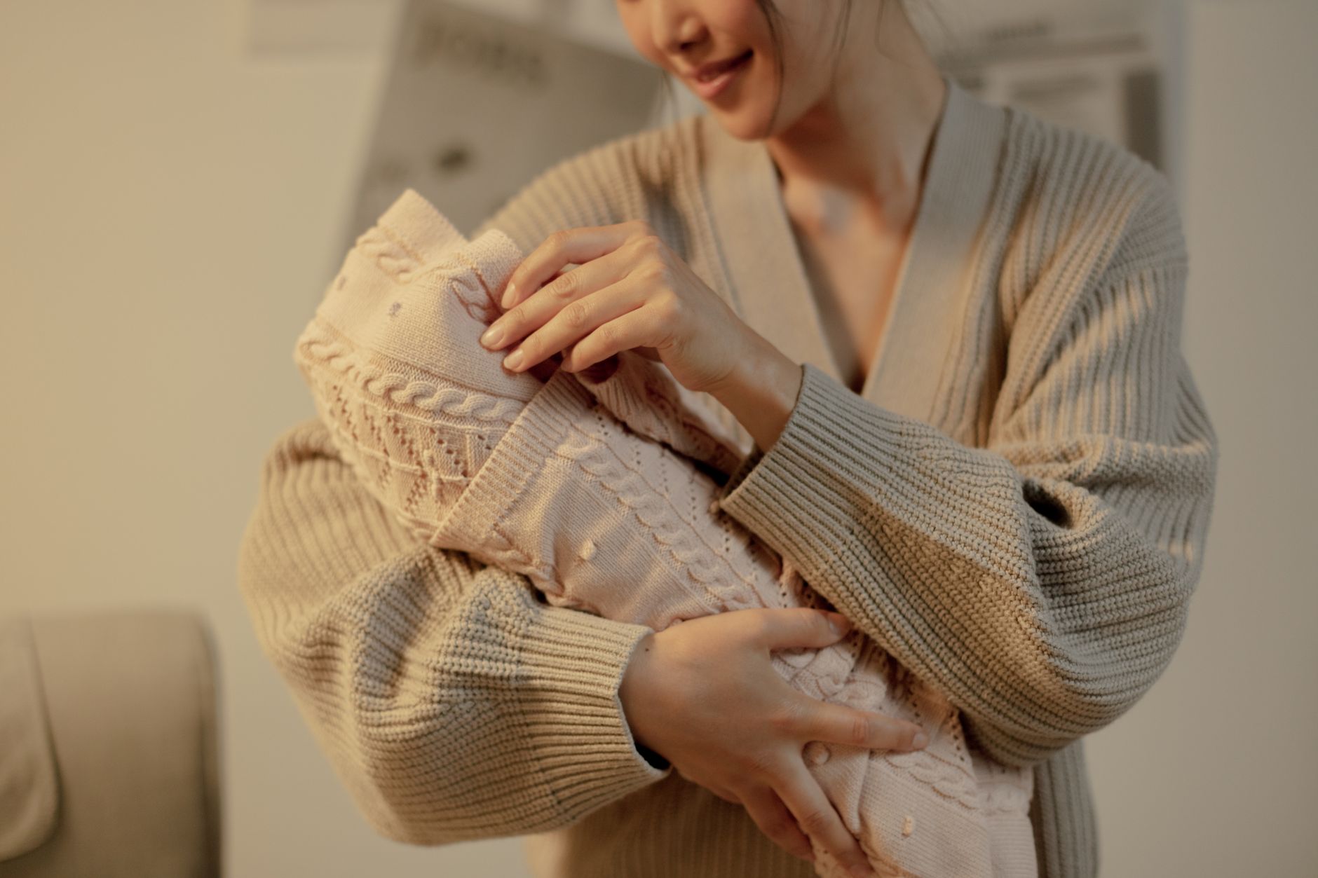 A loving mother cradles her newborn baby wrapped in a soft, knitted blanket indoors, radiating warmth and tenderness.
