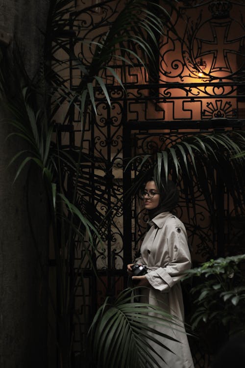 Woman in Trench Coat Standing Beside Green Plant