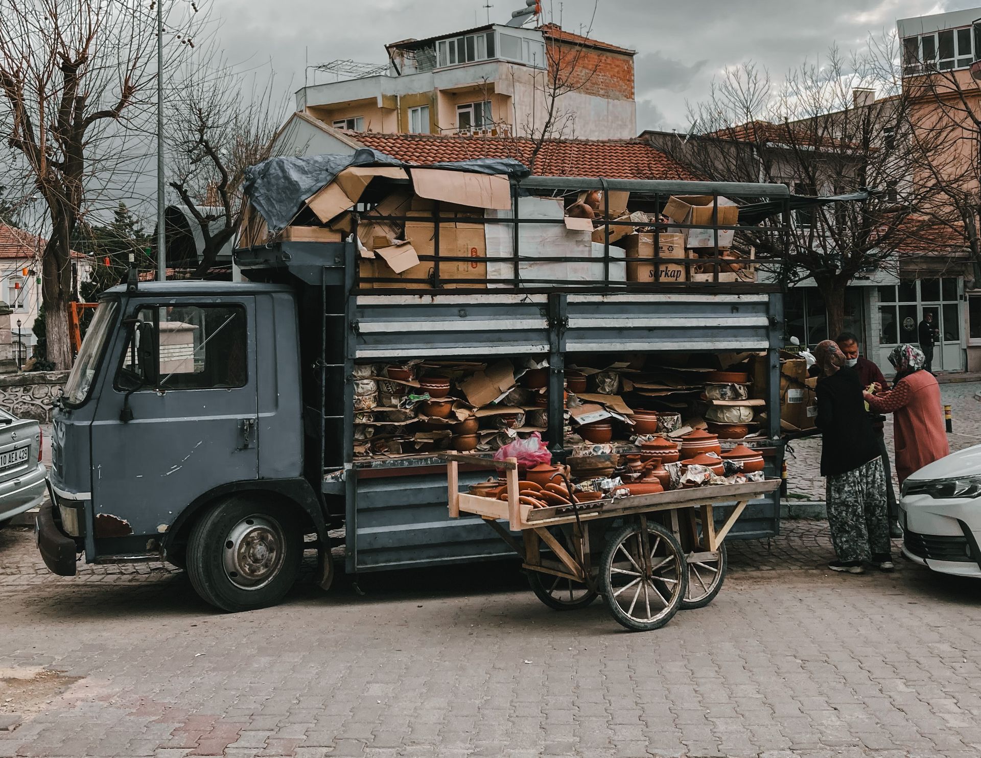 Outdoor market scene with a truck selling pottery and crafts to customers on a city street.