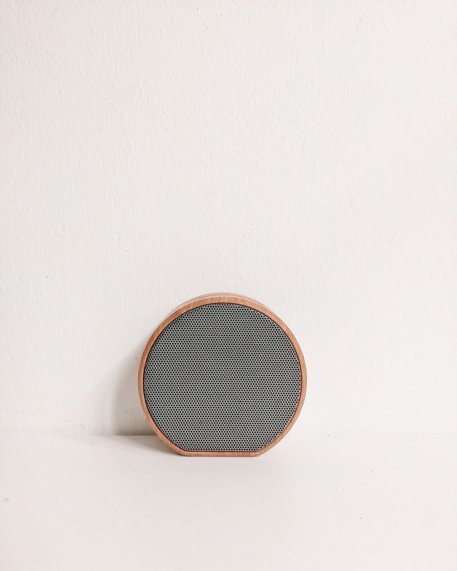 Round wood-framed wireless speaker with a fine mesh grille resting against a pale wall — Kaye RD on Pexels