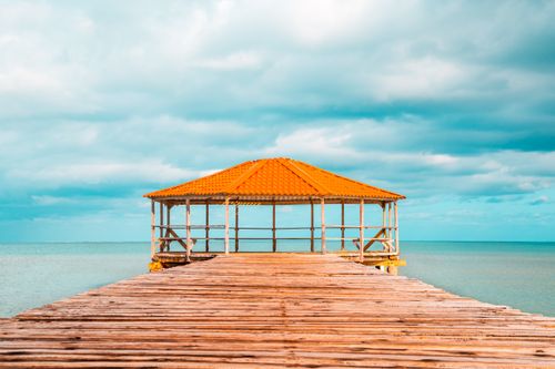 Free Wooden pier leading to a gazebo by the turquoise sea under a vibrant sky. Stock Photo