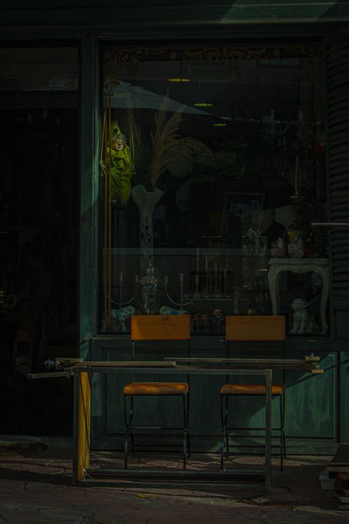 Free A dimly lit antique shop window displaying retro chairs and vintage decor items. Stock Photo