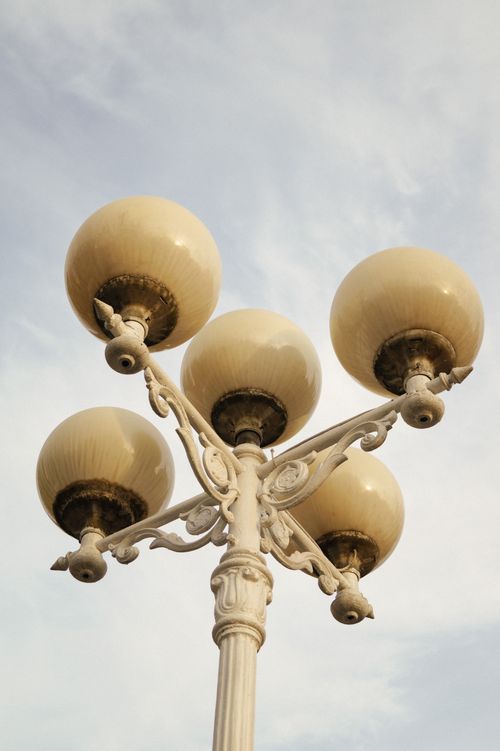 Free A close-up view of an ornate vintage lamppost against a cloudy sky, capturing its elegant design. Stock Photo