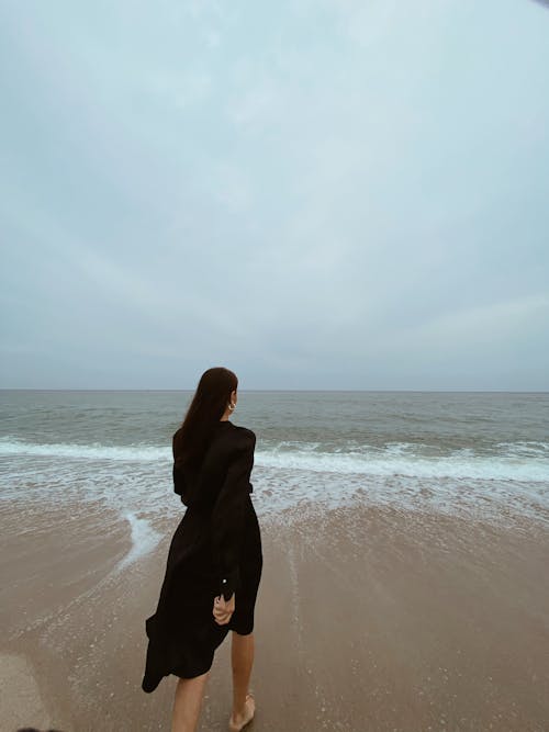 Woman in Black Dress Walking on the Beach