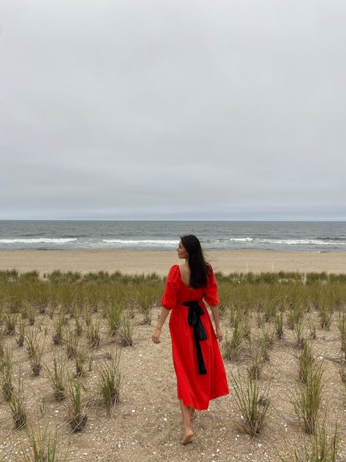 Woman in Red Dress Walking on Sand Near the Beach
