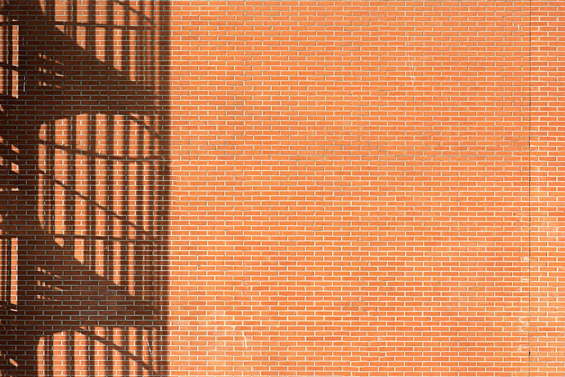 A Light Casting a Shadow of Lines on a Brown Brick Wall