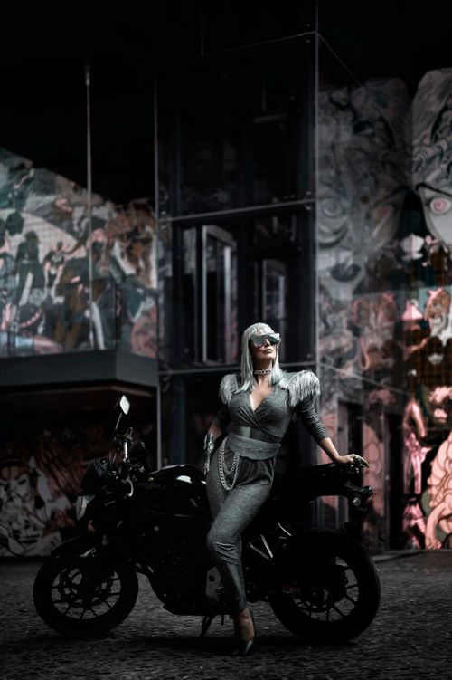 Free Fashionable woman in costume posing with motorcycle amidst urban art backdrop. Stock Photo