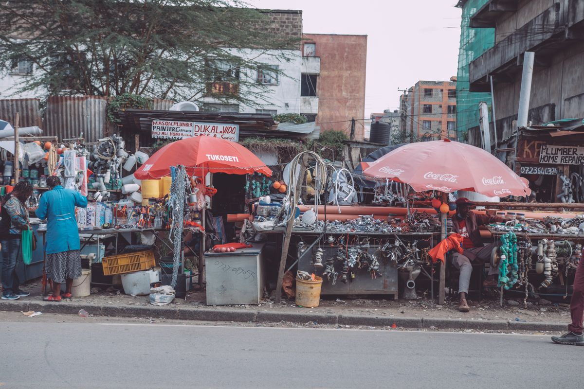 Hardware stalls under red umbrellas at a trading stop along the highway, pipe fittings and spanners laid out where a passing driver can see them.