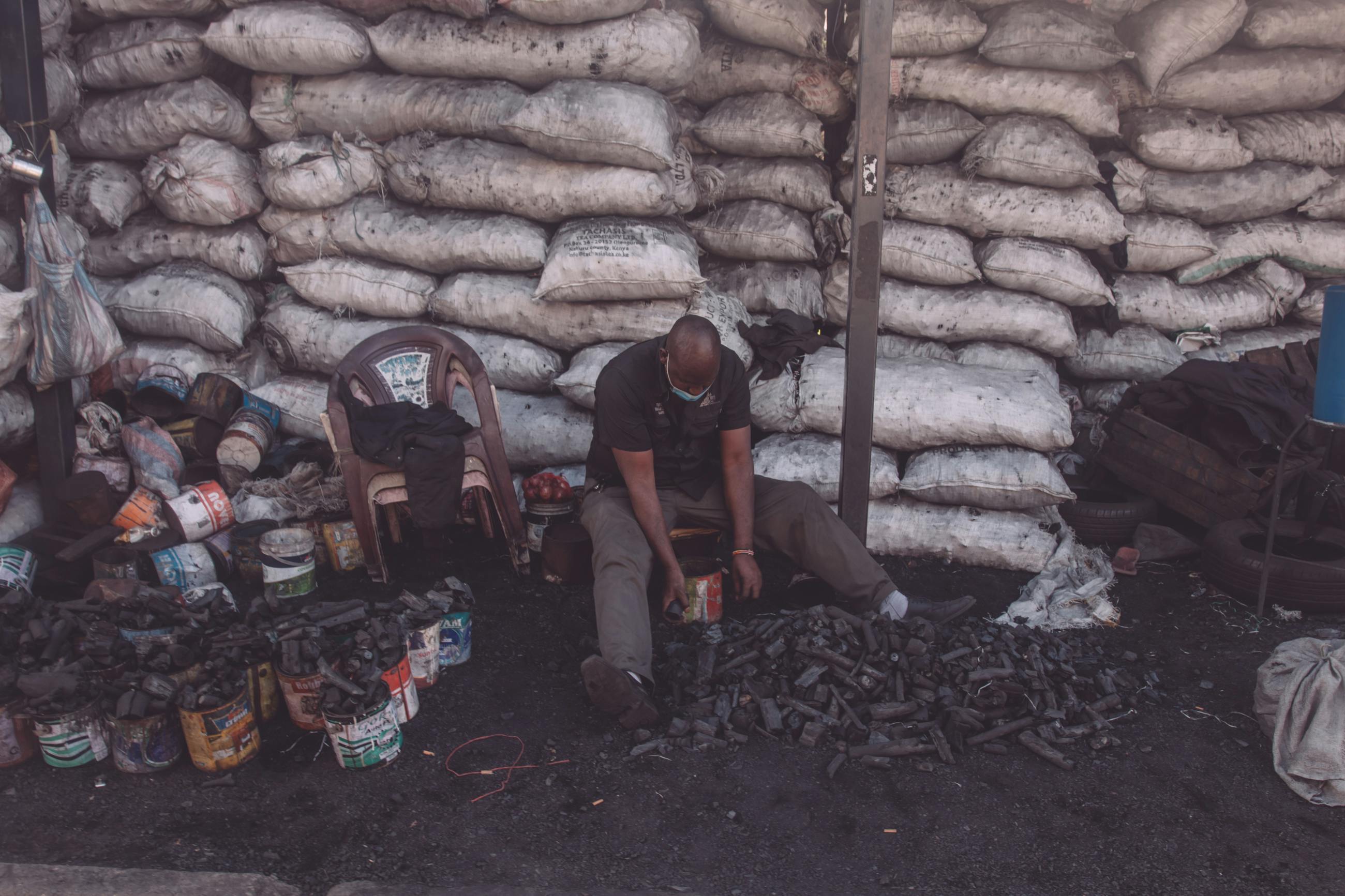 A man sitting and sorting charcoal bags in an outdoor market setting.