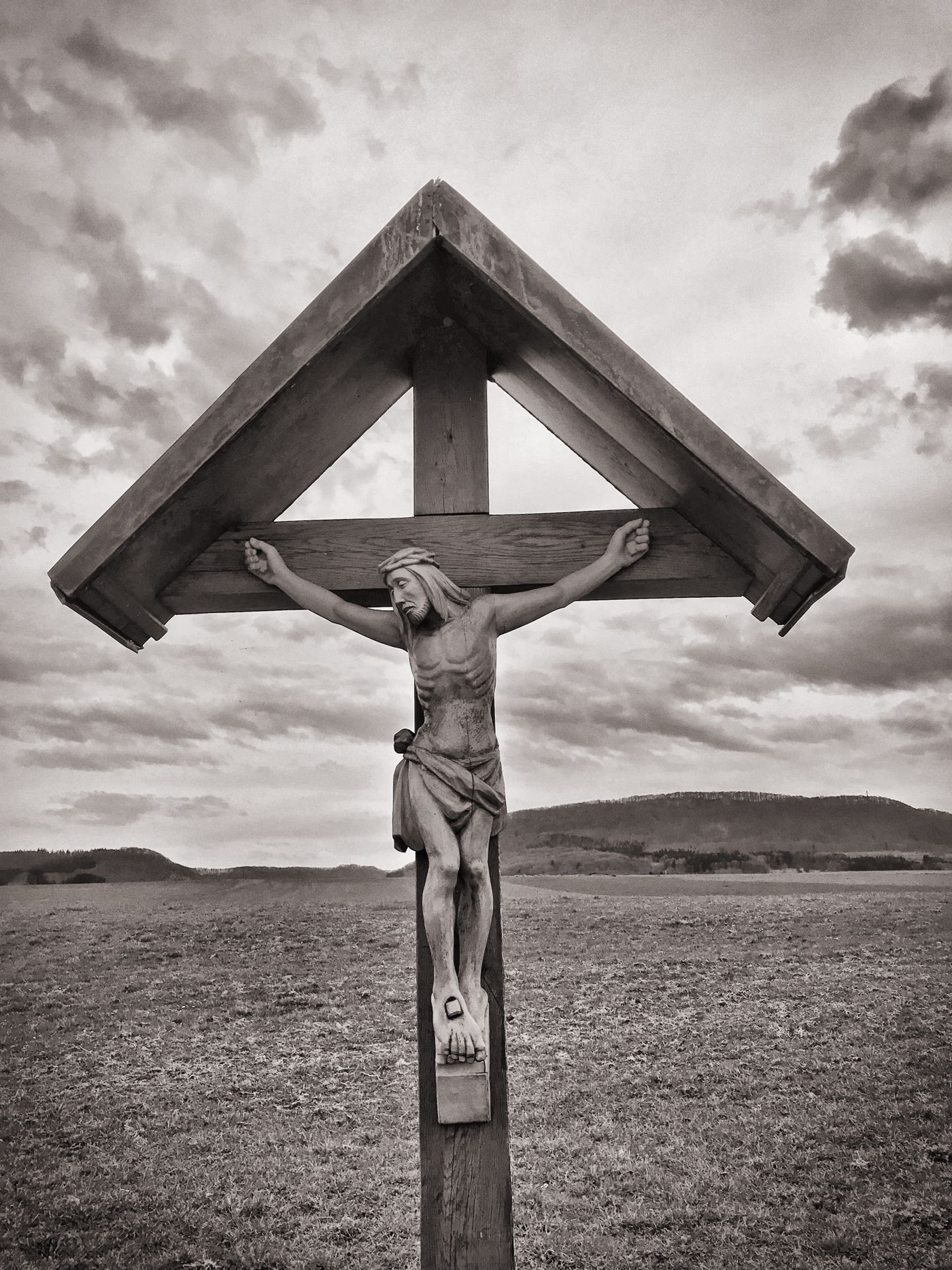Crucifixo de madeira em um campo aberto sob céu nublado, símbolo da fé cristã