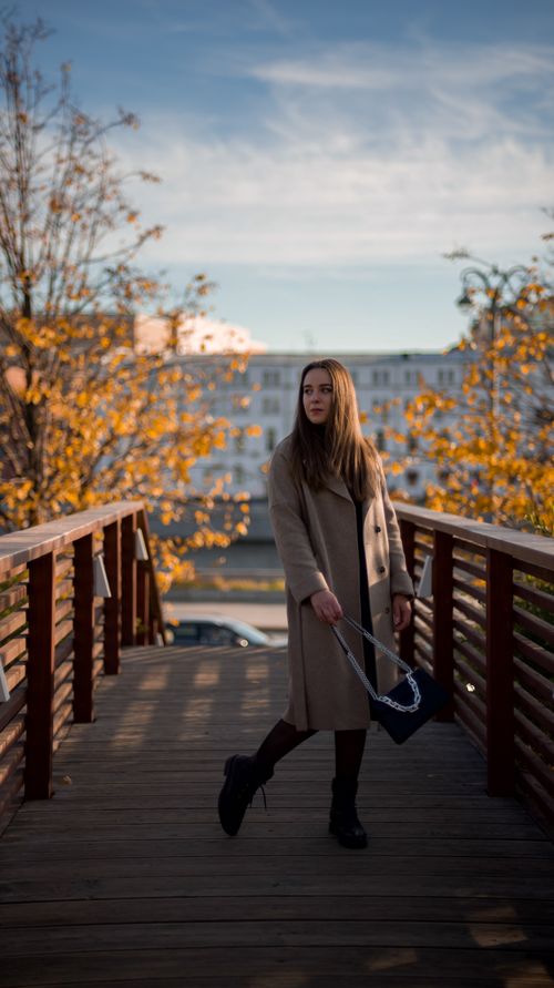 Free Stylish woman walks on a wooden bridge amidst fall foliage, blending fashion with nature. Stock Photo