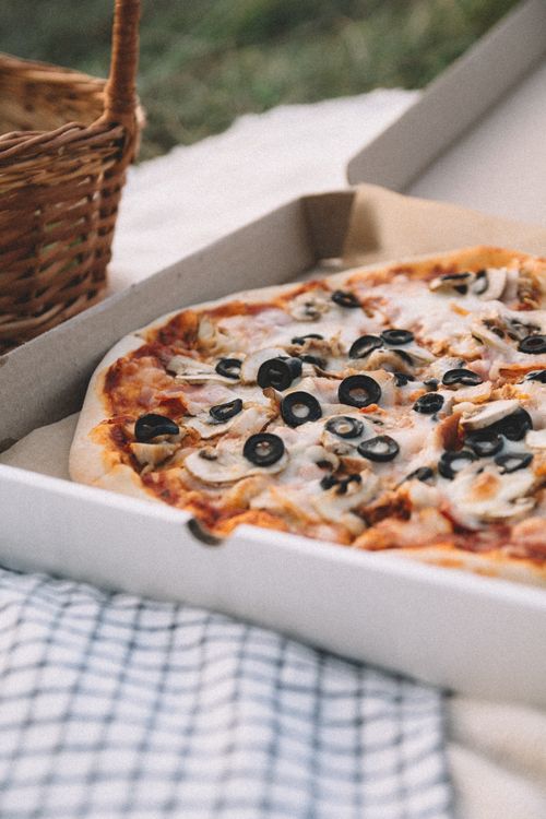 Free Tasty pizza with cheese, olives, and mushrooms in a cardboard box for outdoor picnic. Stock Photo