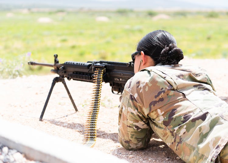 Woman In Military Uniform Aiming An Automatic Rifle