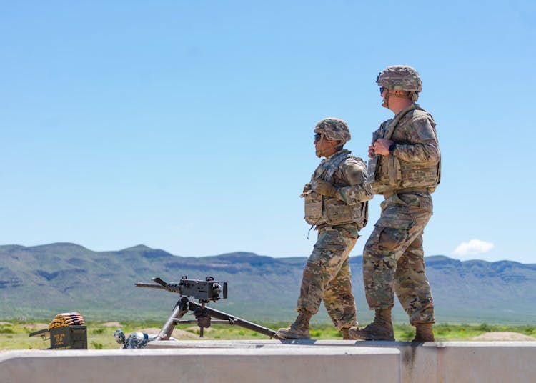 Man In Camouflage Uniform Standing Near An Automatic Weapon