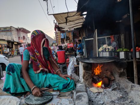 Woman preparing food on open flame at a bustling Jaipur street market.