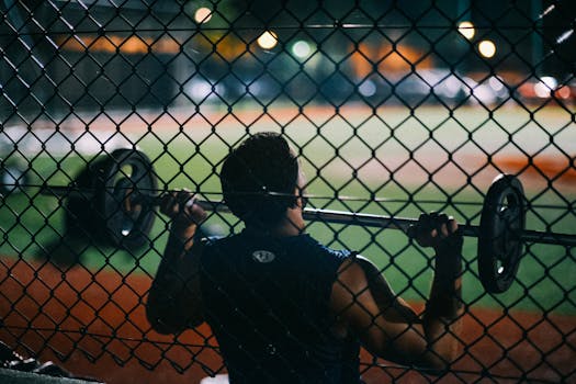 A man lifting weights behind a chain fence at night, showcasing strength and fitness.