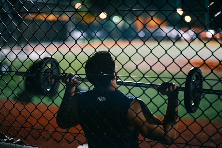 Person Lifting Barbell Behind Chain Fence