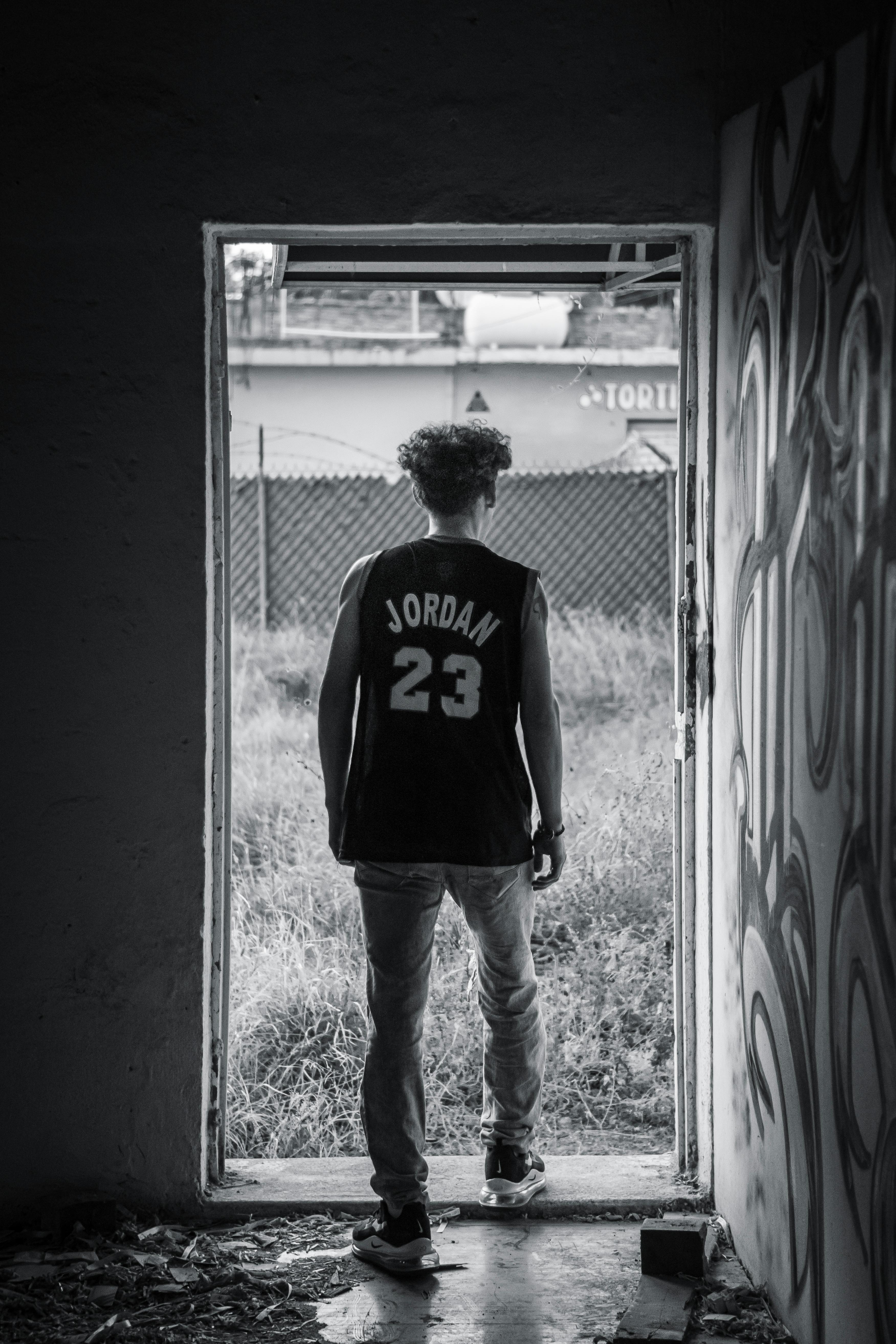 Black and white image of a man in a basketball jersey standing in a doorway, looking out.