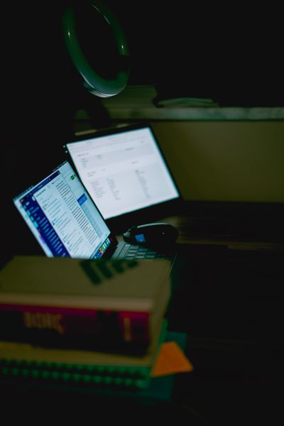 Cozy desk at night with a glowing laptop and stacked books, photo by Sami Abdullah on Pexels
