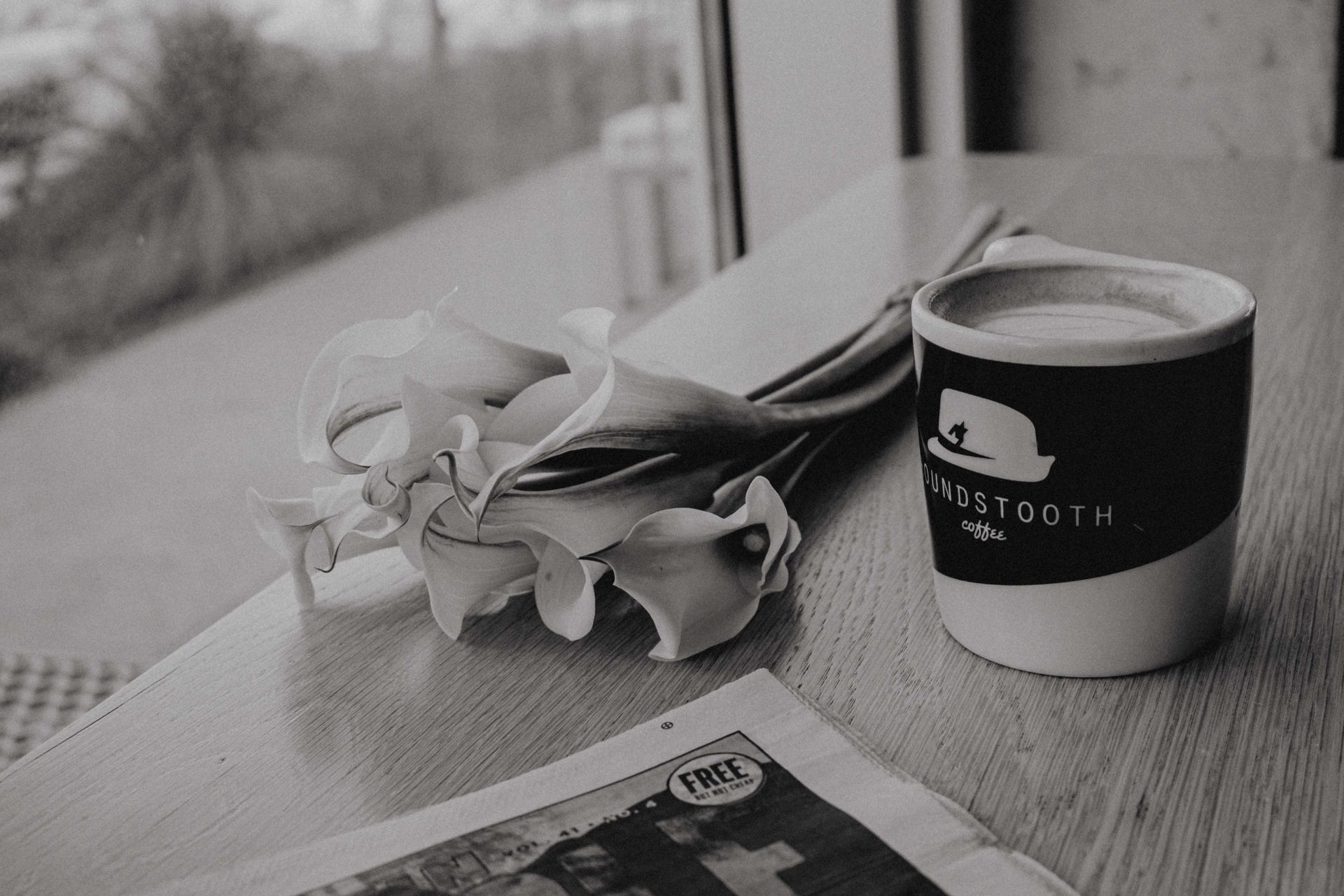 Elegant grayscale coffee scene with calla lilies and a mug on a wooden table.